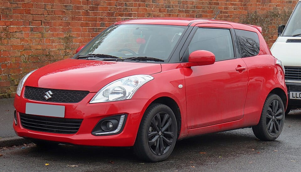 Suzuki Swift 2017-2022 - czerwony hatchback na ulicy, widok z przodu i boku.