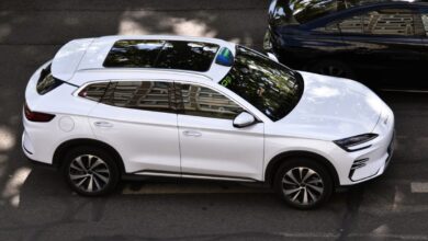 Biały SUV na ulicy, widok z góry, z odbiciem drzew na szybie.